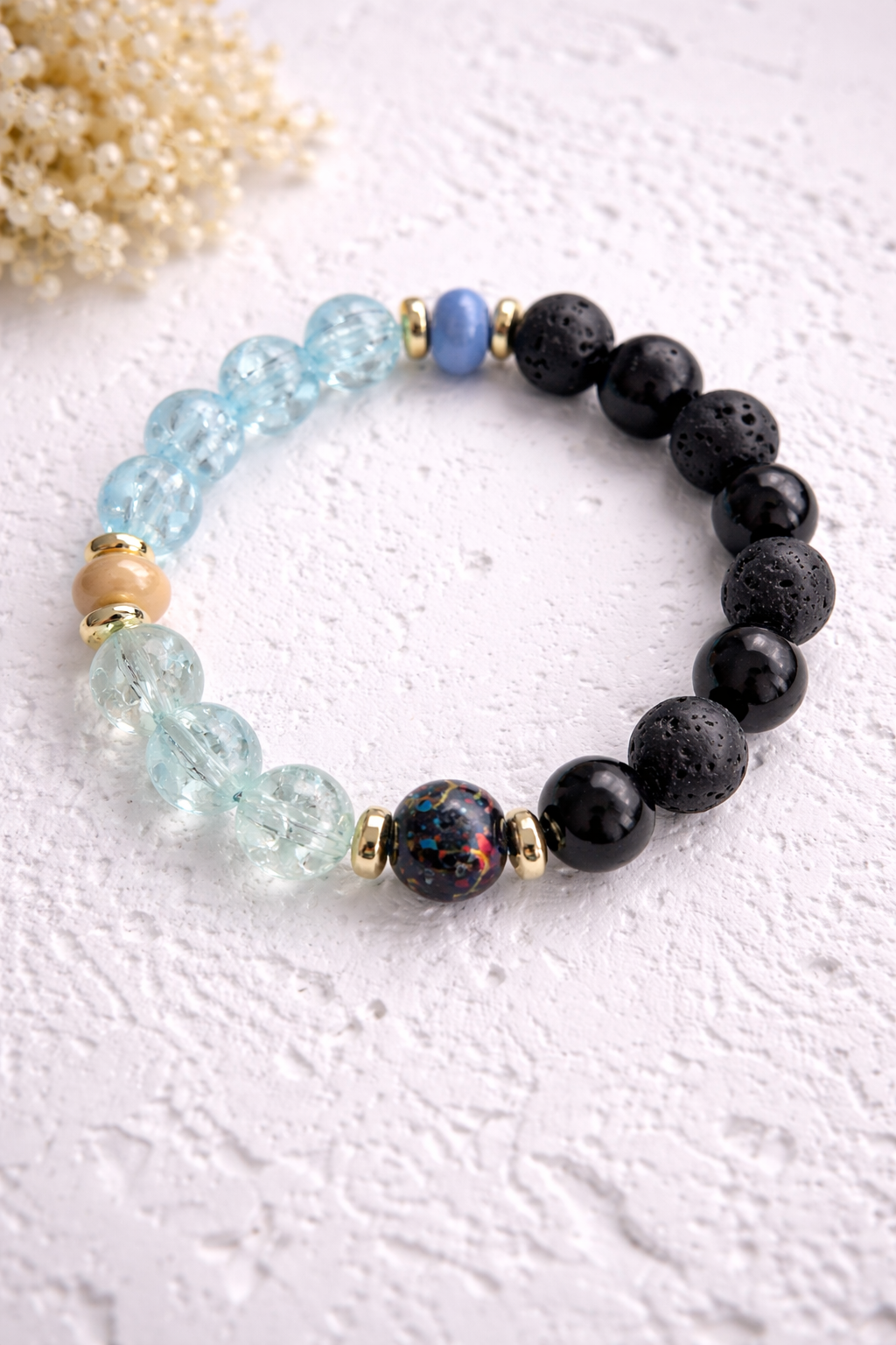 Handgemachtes Lava- & Natursteinarmband mit schwarzen Lavaperlen, blauen Glasperlen und goldfarbenen Akzenten auf hellem Hintergrund