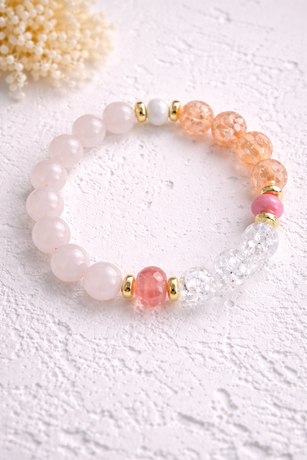 Handgemachtes Rosenquarz-Armband mit pfirsichfarbenen Crackle-Perlen, klaren Glasperlen und goldfarbenen Akzenten auf hellem Hintergrund