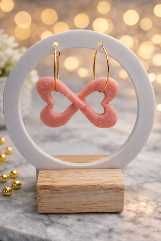 Handgemachte Creolen mit rosa Polymer-Clay-Anhänger in Schleifenform auf Schmuckständer